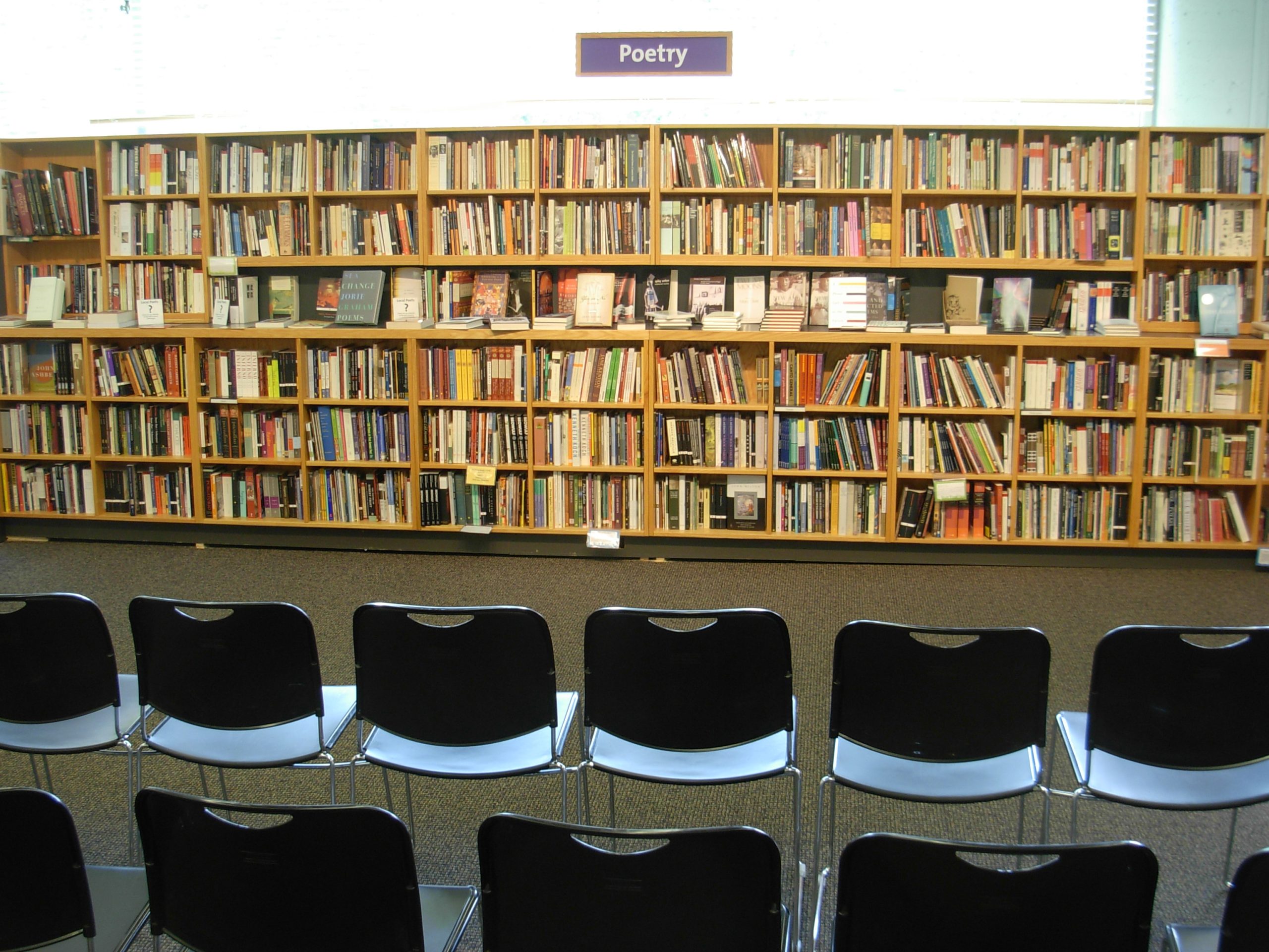 Rows of empty chairs face a wall of poetry books in a bookstore, set out for a reading.