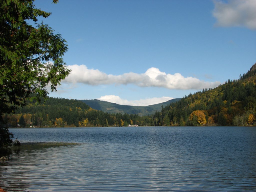 Silver Lake in Whatcom County: calm blue water below forested hills in autumn color, with a long white cloud over the far ridge